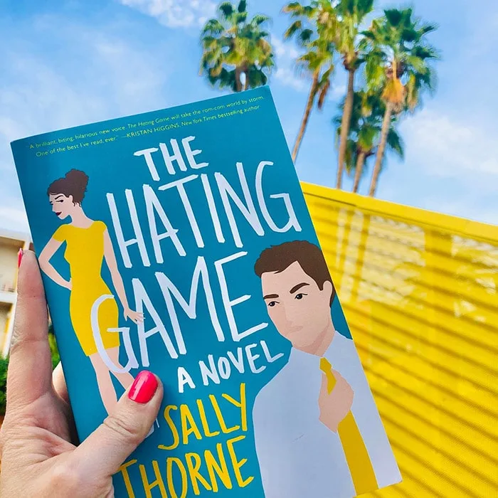 The Hating Game novel cover in front of palm trees and blue skies