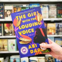Girl with the Louding Voice purple book cover held in front of book shelf