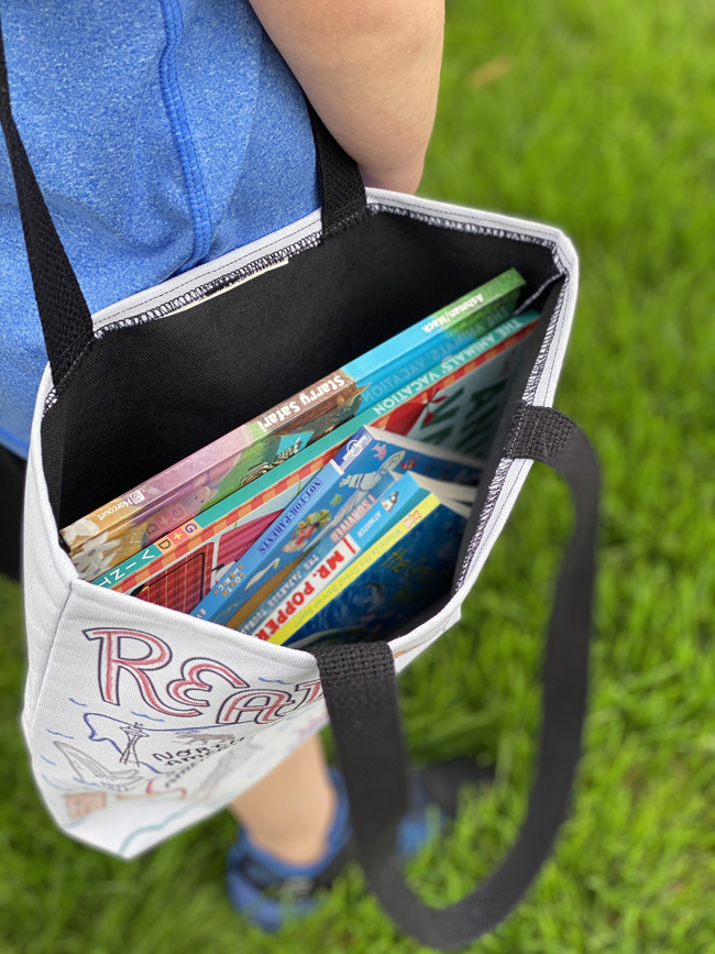 child with library book tote full of books