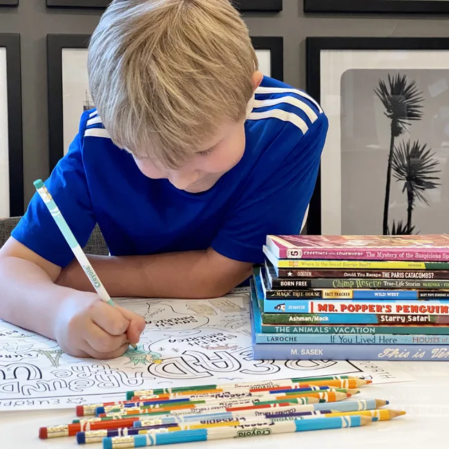 Boy coloring large world map poster with colored pencils and stack of books