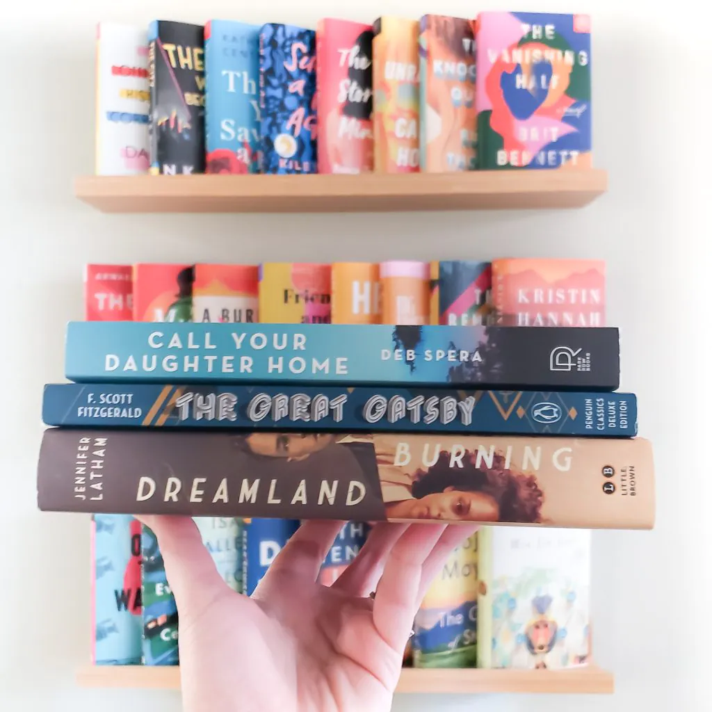 Stack of 3 books in a hand, in front of a wall of books 