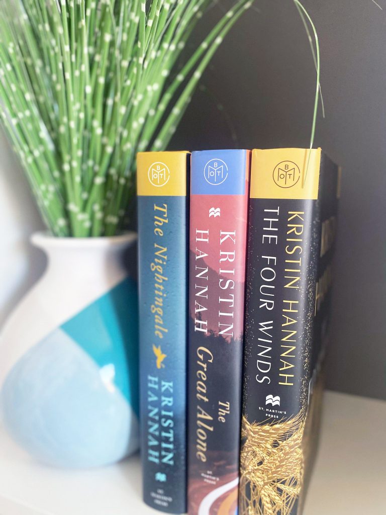 Photo of three of Kristin Hannah's best books - The NIghtingale, The Great Alone, and the Four Winds - next to a vase of greenery