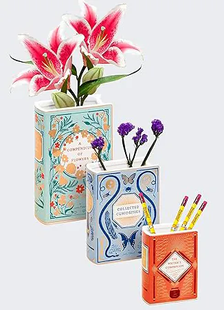 Three ceramic book vases, two filled with flowers and one holding pencils