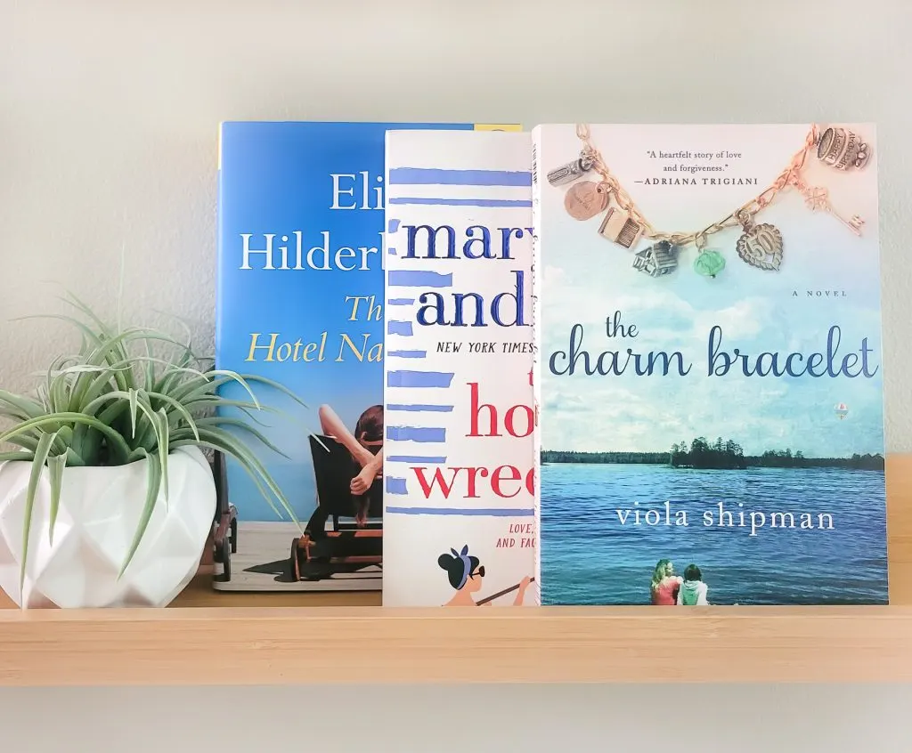 Three overlapping beach read books facing forward on a shelf next to a small succulent in a white pot. The books are The Hotel Nantucket, The Homewreckers, and The Charm Bracelet.