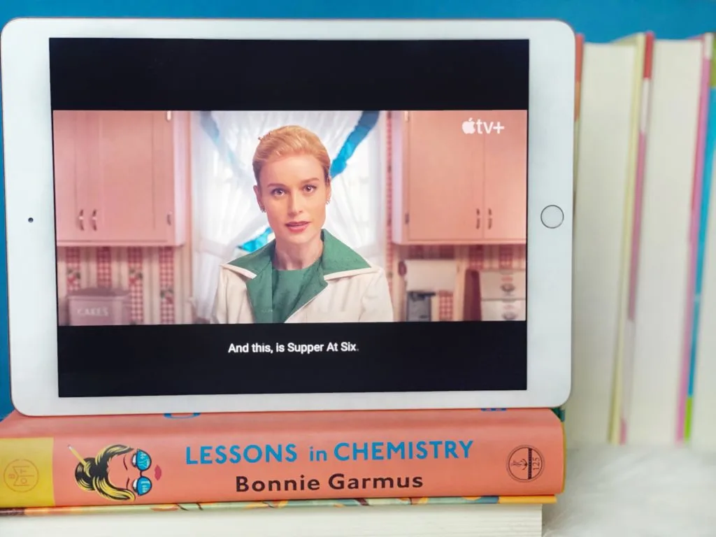 Apple TV preview of Lessons in Chemistry on the screen of an iPad. The iPad is standing on top of the Lessons in Chemsitry book.