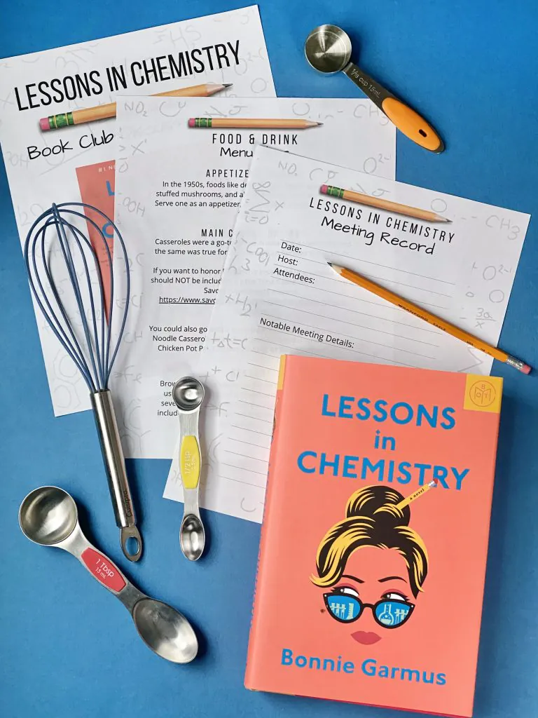 Three pages from the Lessons in Chemistry Book Club Kit along with book. A kitchen whisk and three measuring cups and spoons are scattered around the edges of the photo.