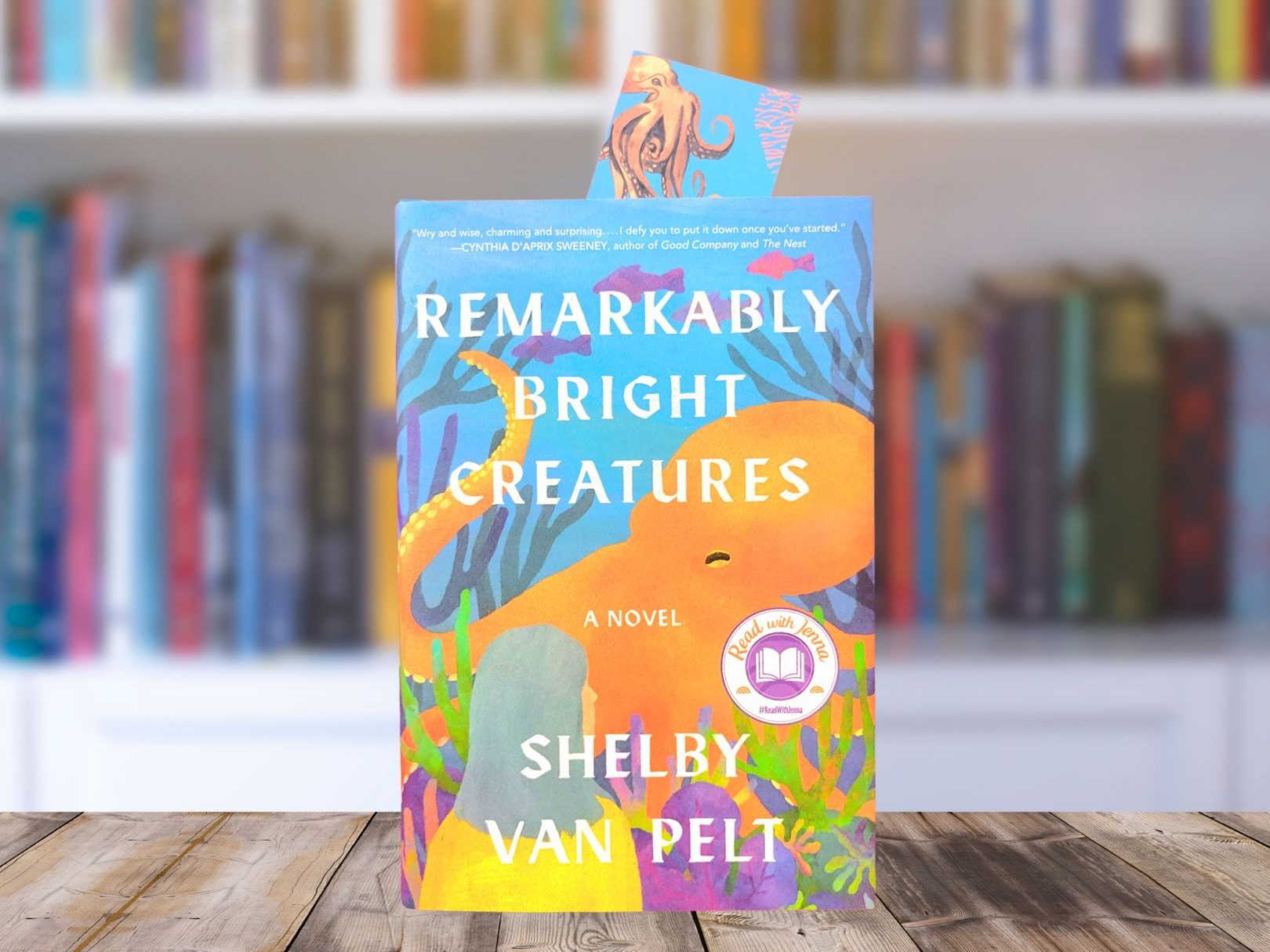 Book cover for Remarkably Bright Creatures featuring bright colors and an orange octopus, sitting on a table in front of a bookcase
