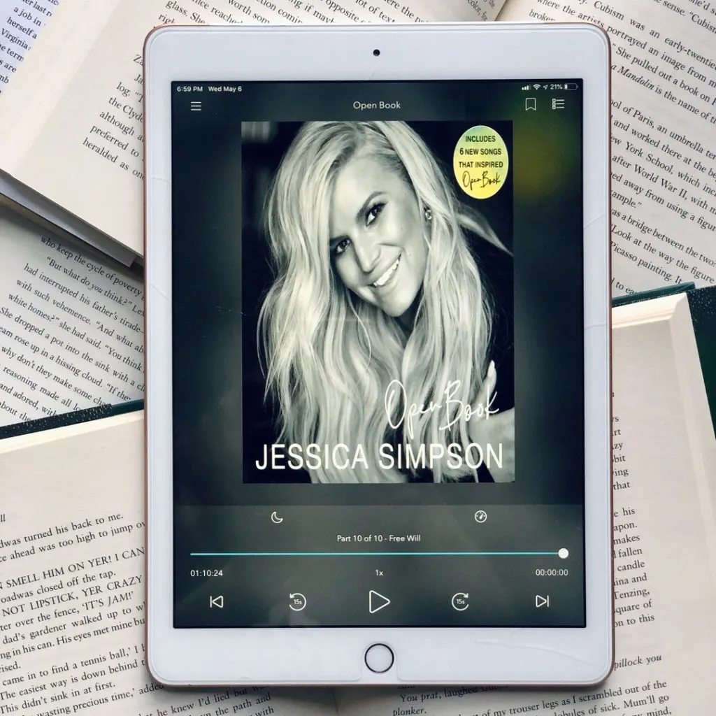 The audiobook of Jessica Simpson's memoir Open Book on an iPad screen. The iPad is sitting on top of a stack of open books.