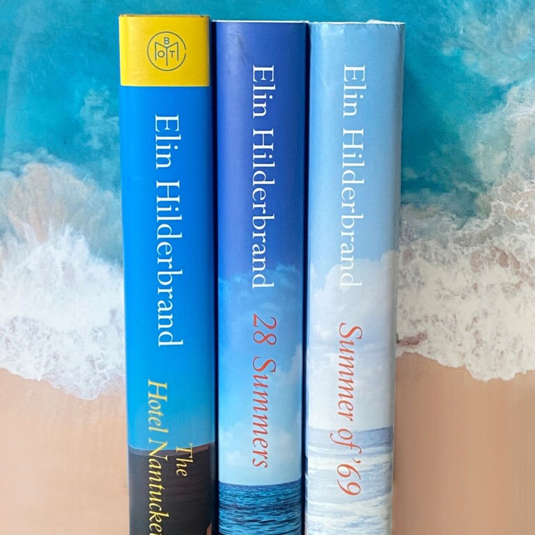 Three blue Elin Hilderbrand book spines on a background image of ocean waves and sand