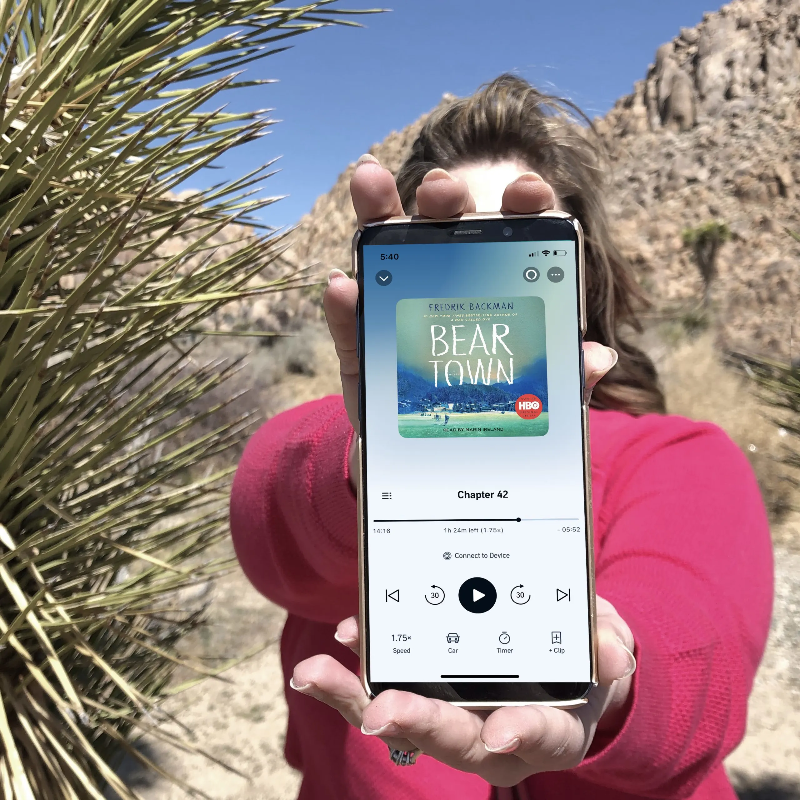 Photo of a woman holding an iPhone with an Audible book on the screen for a post called How Does Audible Work