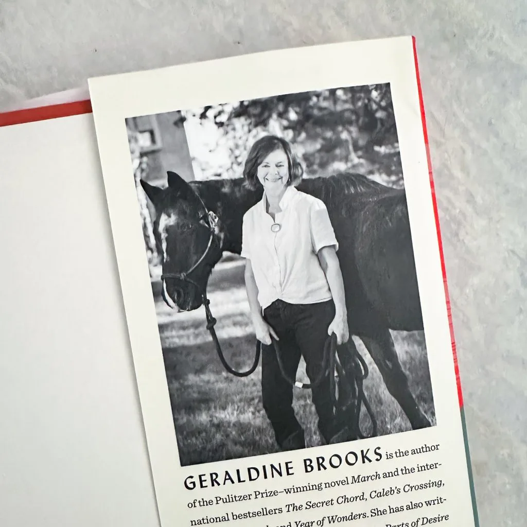 Author photo of Geraldine Brooks in white shirt standing in front of a Horse
