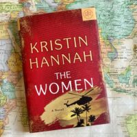 A hardback copy of The Women by Kristin Hannah laying on top of a world map with Vietnam in view to the right of the book