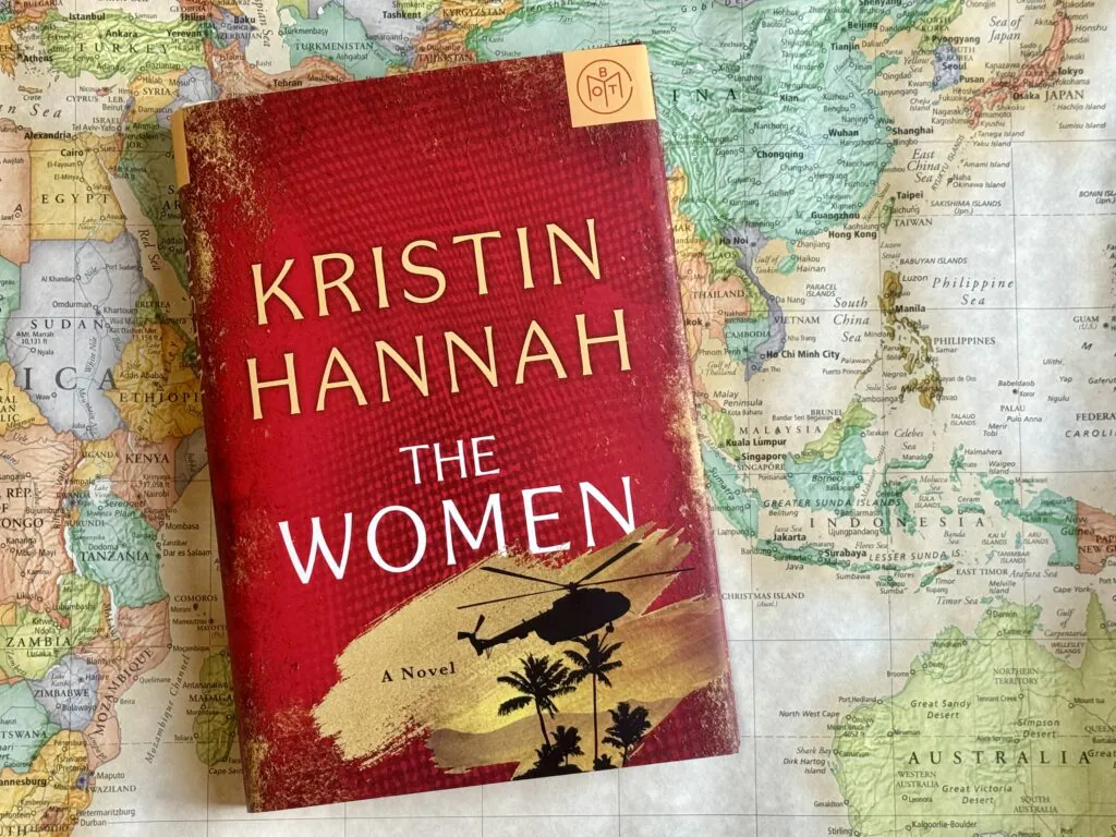 A hardback copy of The Women by Kristin Hannah laying on top of a world map with Vietnam in the center of the image