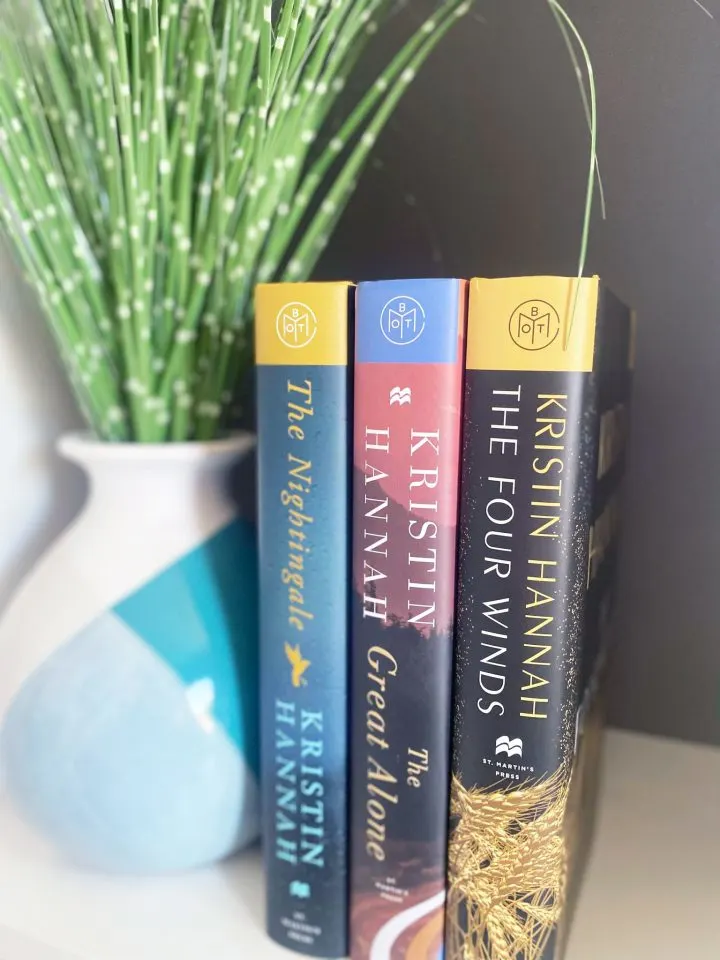 Photo of three Kristin Hannah book spines next to a teal and white vase filled with greenery