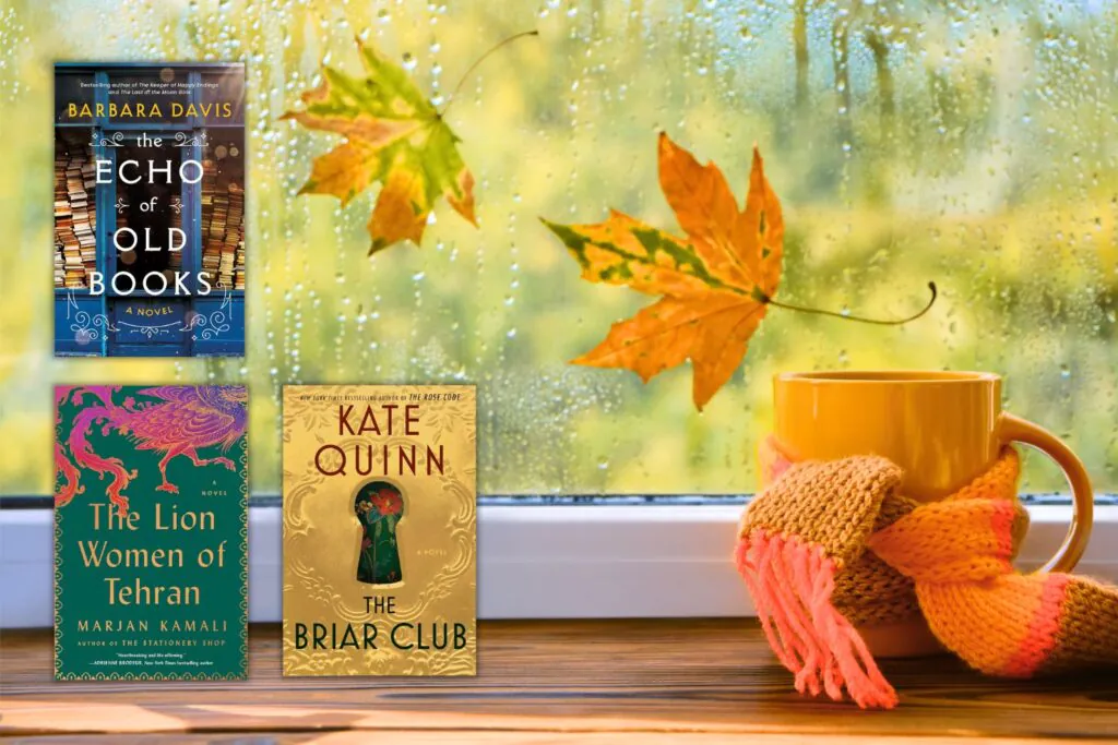 Three books in front of window with falling leaves and orange cup of coffee