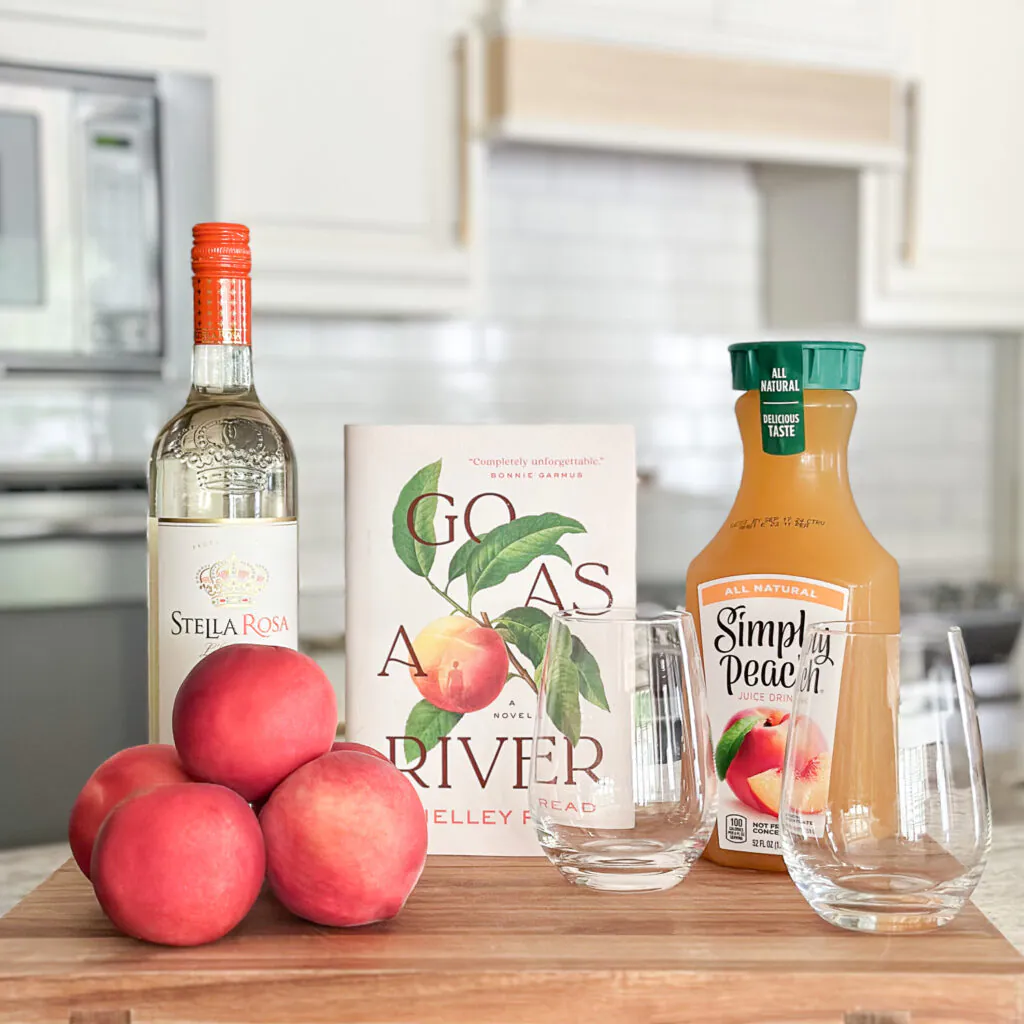 Go As a River book standing on a wood block with peaches, peach wine, and peach juice