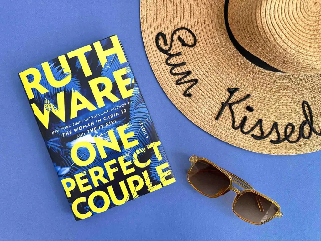 One Perfect Couple by Ruth Ware book with Sunhat and Sunglasses on Blue Background