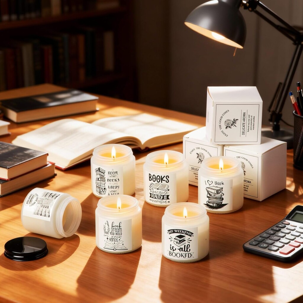 A collection of jar candles with bookish labels sitting on a wood desk with books, a calculator, and a lamp.