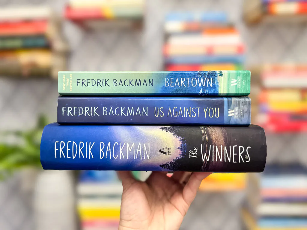 A hand holding all three books in Fredrik Backman's Beartown Trilogy