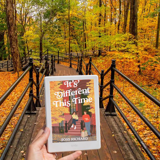 Square photo of a wooden walkway surrounded by trees and fall leaves and a hand holding out a Kindle displaying a fall book cover