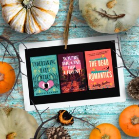An ipad with three Halloween romance covers on the screen surrounded by pumpkins all laying on a blue wood background