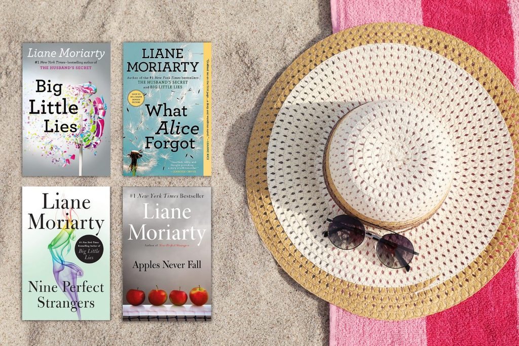 White beach hat on pink towel and sand with 4 Liane Moriarty Books