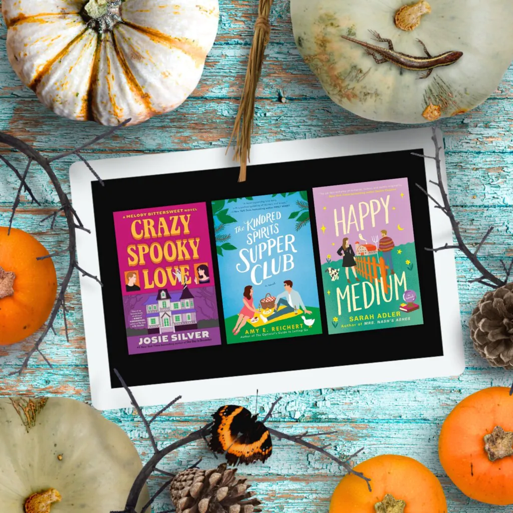 An ipad with three Halloween romance covers on the screen surrounded by pumpkins all laying on a blue wood background