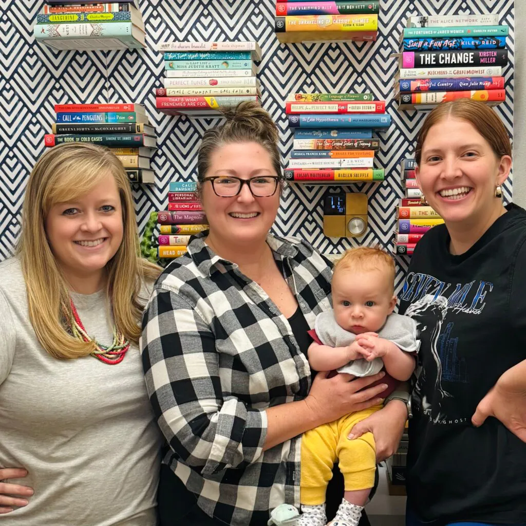 Three women and a baby in front of a wall of books